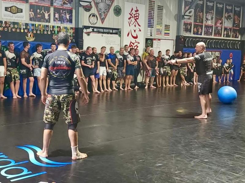 Adults in rash guards and shorts lined up along the wall during a BJJ No Gi class