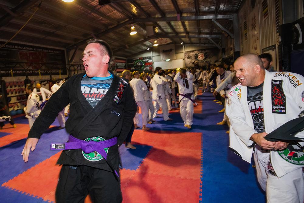 A new purple belt running the gauntlet between two lines of teammates swinging their belts on grading night