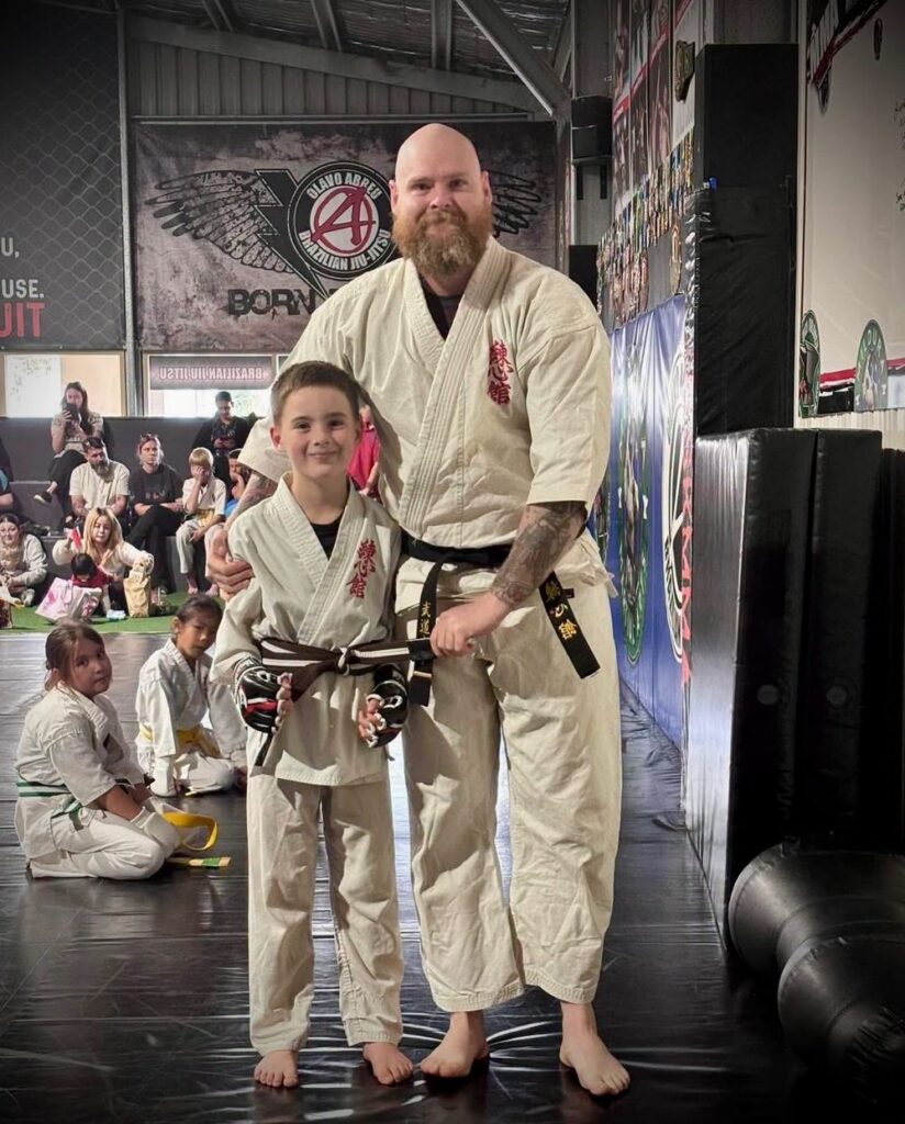 A young karate student holding his new belt beside his instructor on grading day