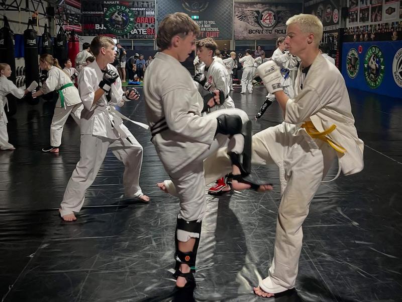 Two kids in karate uniforms practising knee strikes with pads