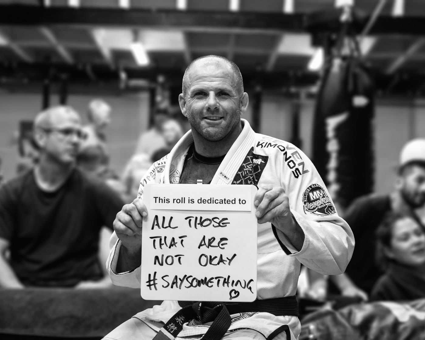 Mick Moloney in his gi holding a sign that reads: This roll is dedicated to all those that are not okay, #SaySomething