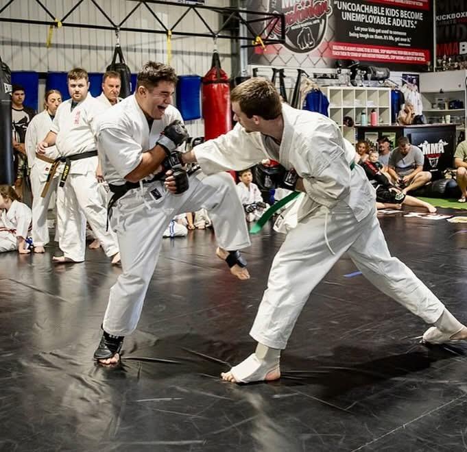 Two students in karate uniforms sparring with MMA gloves