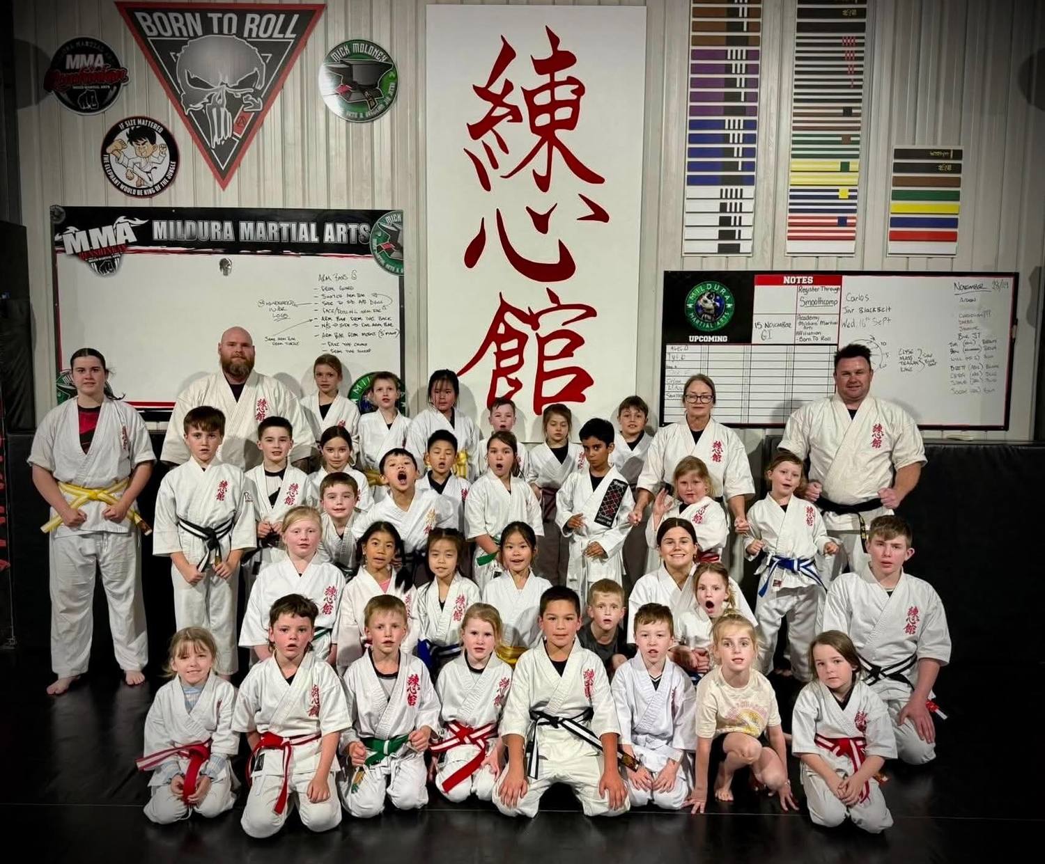 The kids karate class in white uniforms with their instructors under the Renshinkan sign